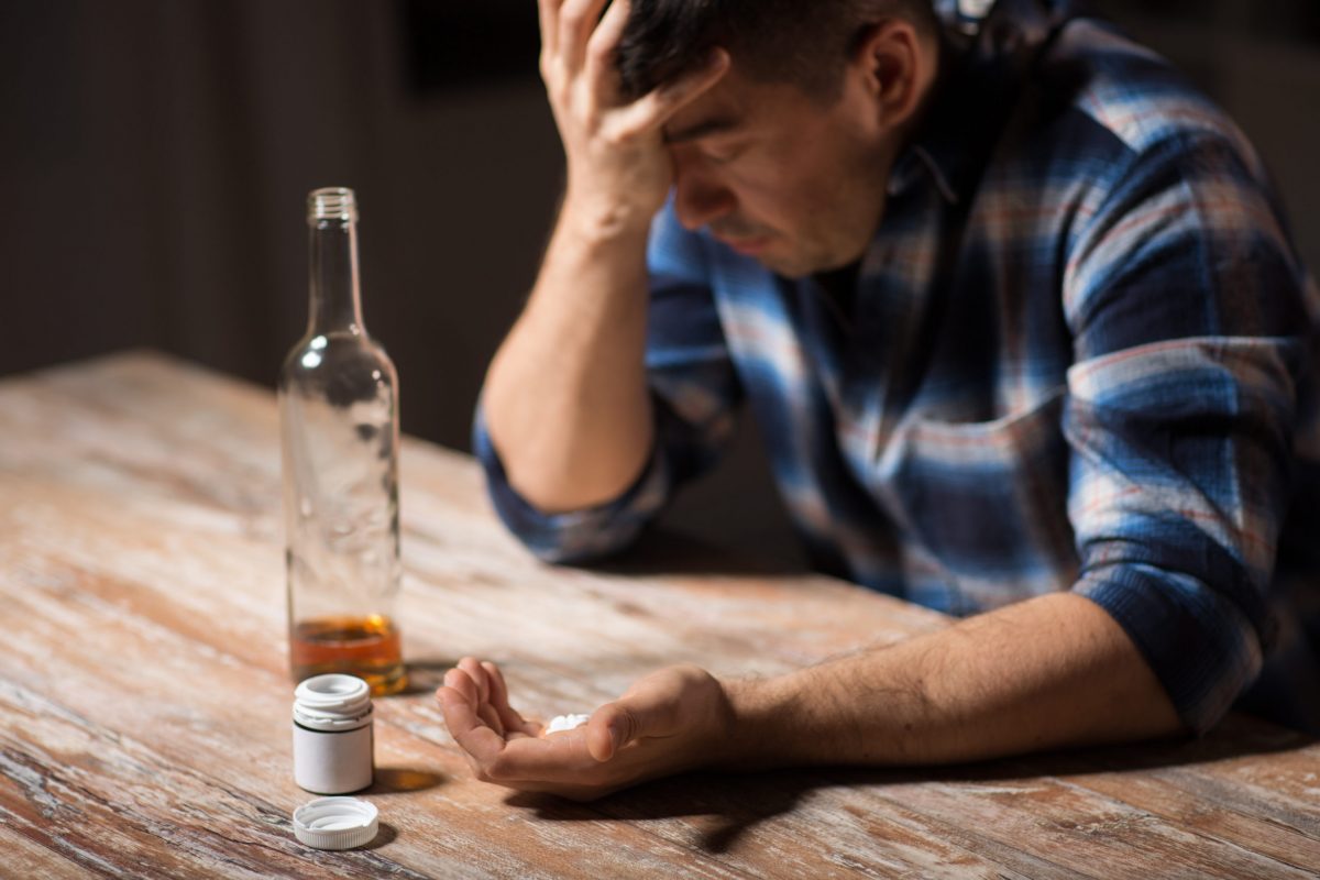 unhappy drunk man with bottle of alcohol and pills