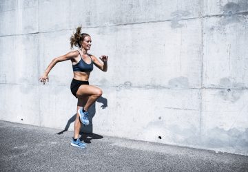 a fit woman doing high knee workout outside against a grey wall background