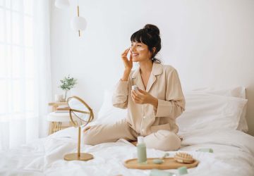 a woman putting skin care products on while sitting in bed