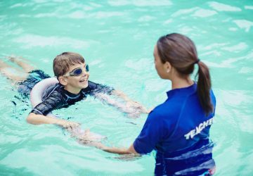 a swim instructor teaching a young boy with goggles to swim